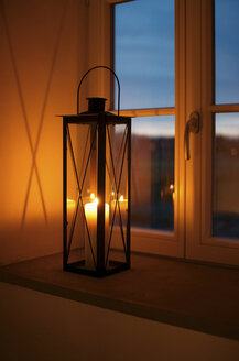 Lantern with lighted candle on window sill at dusk - HAWF000016