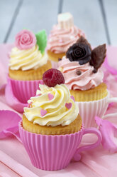 Vier Backformen in Form von Tassen mit dekorierten Cupcakes auf rosa Krepppapier - CSF021173