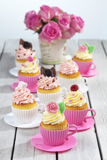 Backformen in Form von Tassen mit dekorierten Cupcakes und Rosen auf Holztisch - CSF021174