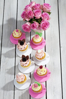 Backformen in Form von Tassen mit dekorierten Cupcakes und Rosen auf Holztisch, Blick von oben - CSF021181