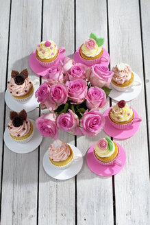 Backformen in Form von Tassen mit dekorierten Cupcakes und Rosen auf Holztisch, Blick von oben - CSF021183