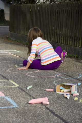 Girl drawing with coloured crayon on asphalt stock photo