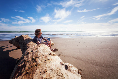 Neuseeland, Wanganui Strand, Junger Mann sitzt am Strand, lizenzfreies Stockfoto