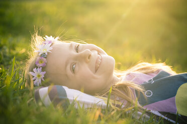 Portrait of smiling little girl lying on meadow wearing flowers - SARF000429