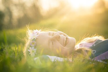 Portrait of laughing little girl lying on meadow wearing flowers - SARF000430