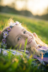 Porträt eines lächelnden kleinen Mädchens, das auf einer Wiese liegt und Blumen trägt - SARF000431