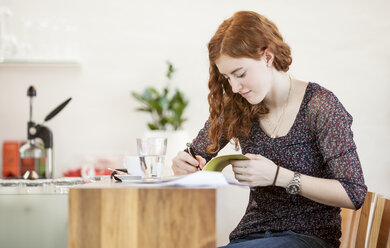 Junge Frau mit Notizbuch schreibt in einem Café - DISF000717