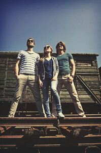 Drei Freunde mit Sonnenbrillen stehen vor einem alten Güterwagen - HOHF000664