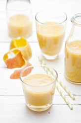 Gläser und Flaschen mit Mango-Bananen-Smoothie auf weißem Holztisch - CZF000143