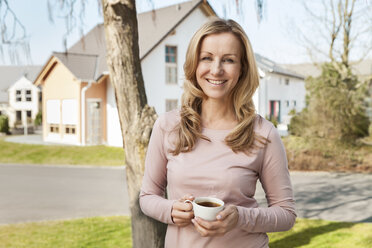 Lächelnde Frau mit einer Tasse Kaffee vor einem Wohngebiet stehend - MFF000968