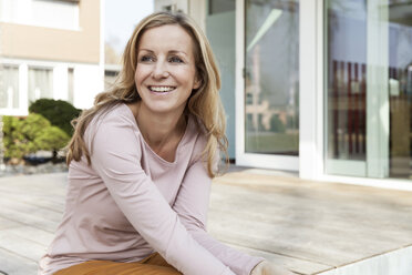 Lächelnde Frau sitzt auf der Terrasse eines Wohnhauses - MFF000977