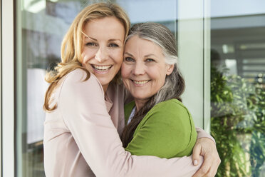 Senior mother and her daughter hugging in front of her house - MFF000982