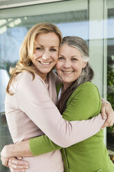 Senior mother and her daughter hugging in front of her house - MFF000983