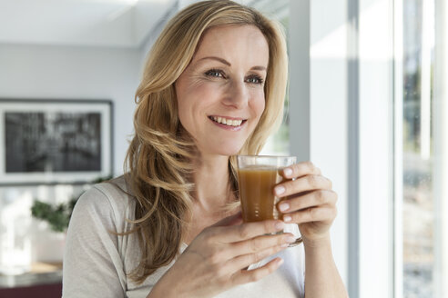 Porträt einer glücklichen Frau mit Getränk in ihrem hellen, modernen Haus - MFF000991