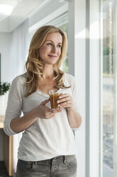 Portrait of happy woman with beverage standing in her bright modern home - MFF000958