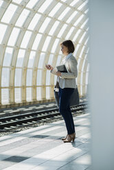 Geschäftsfrau mit Smartphone und Tablet-Computer wartet auf dem Bahnsteig - UUF000124