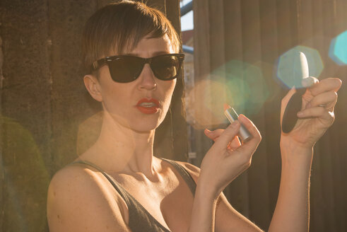Deutschland, Berlin, Porträt einer Frau mit Sonnenbrille, die Lippenstift aufträgt - FBF000318