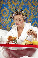 Frau mit Lockenwicklern und weißem Bademantel beim Frühstück im Bett - CSBF000005