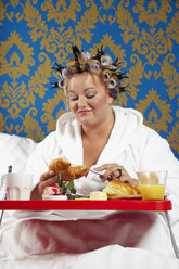 Frau mit Lockenwicklern und weißem Bademantel beim Frühstück im Bett - CSBF000006