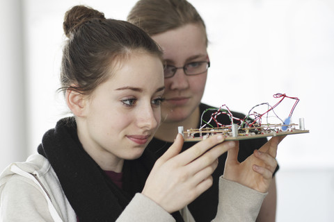 Zwei junge Frauen halten ein Bauteil eines optischen Sensors in einer Elektronikwerkstatt, lizenzfreies Stockfoto