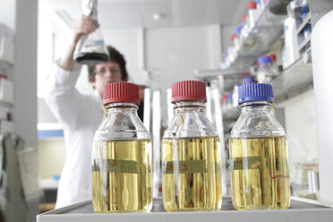 Labortechniker hält Algakulturflasche, Wachstumsmediumflaschen im Vordergrund - SGF000526
