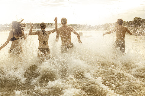 Four friends running into quarry pond stock photo