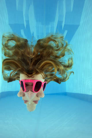 Mädchen mit Sonnenbrille schaut durch die Wasseroberfläche, lizenzfreies Stockfoto
