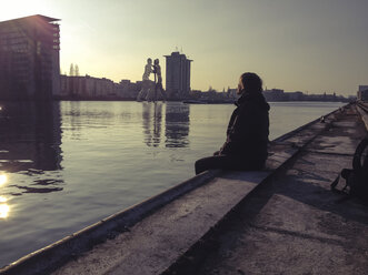 Germany, Berlin, Treptow, young man sitting on pier at sunset - FBF000340