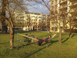 Deutschland, Berlin, Junge Frau sitzt in Hängematte im Monbijou-Park und liest - FBF000319