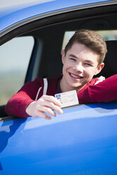 Teenager sitting in car showing driving license, partial view - UUF000175