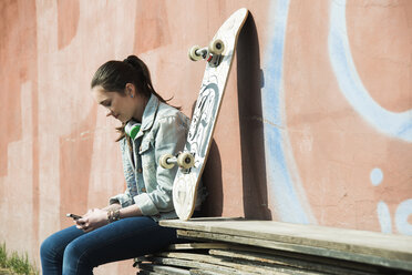 Teenage girl with skateboard using smartphone - UUF000180