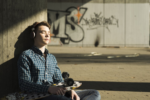 Jugendlicher mit Skateboard hört Musik, lizenzfreies Stockfoto