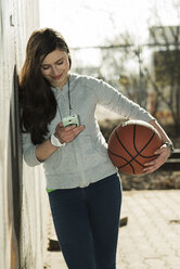 Teenage girl with basketball using smartphone - UUF000170