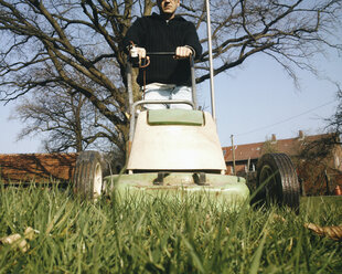 Deutschland, Nordrhein-Westfalen, Petershagen, Mann mäht einen Rasen mit einem alten elektrischen Rasenmäher. - HAWF000088