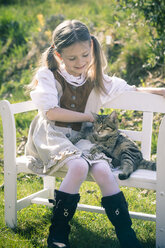 Portait of little girl sitting on wooden bench with cat - SARF000473