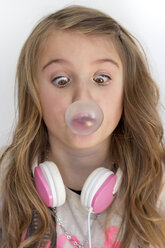 Girl with headphones peering at chewing gum bubble - YFF000096