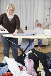 Woman ironing shirt with man in background leaning back - ECF000547