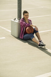 Young woman sitting with basketball outdoors - UUF000243