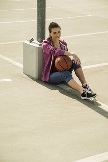 Junge Frau sitzt mit Basketball im Freien - UUF000243
