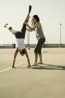 Young woman practicing handstand assisted by a friend - UUF000254