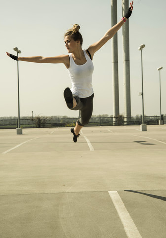 Junge Frau springt in der Luft auf einem Parkdeck, lizenzfreies Stockfoto