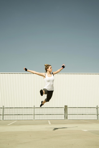 Junge Frau springt in der Luft auf einem Parkdeck, lizenzfreies Stockfoto