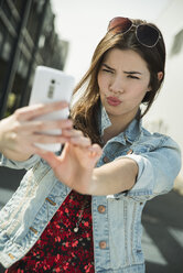 Grimassen schneidende junge Frau, die ein Selfie im Freien macht - UUF000272