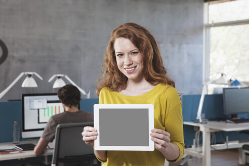 Porträt eines lächelnden Mannes, der einen Tablet-Computer im Büro zeigt - RBF001612