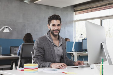 Porträt eines lächelnden Mannes an seinem Arbeitsplatz im Büro - RBF001617