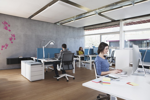 Drei Kollegen arbeiten in einem modernen Großraumbüro, lizenzfreies Stockfoto