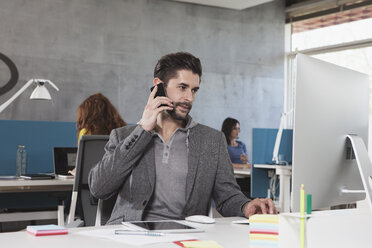 Porträt eines Mannes, der mit seinem Smartphone an seinem Arbeitsplatz im Büro telefoniert - RBF001621