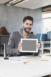 Porträt eines lächelnden Mannes, der einen Tablet-Computer im Büro zeigt - RBF001622