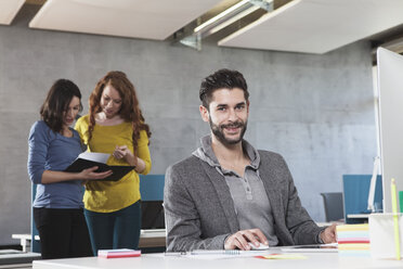 Porträt eines lächelnden Mannes an seinem Arbeitsplatz im Büro - RBF001623