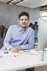 Portrait of smiling man at his workplace in the office - RBF001627